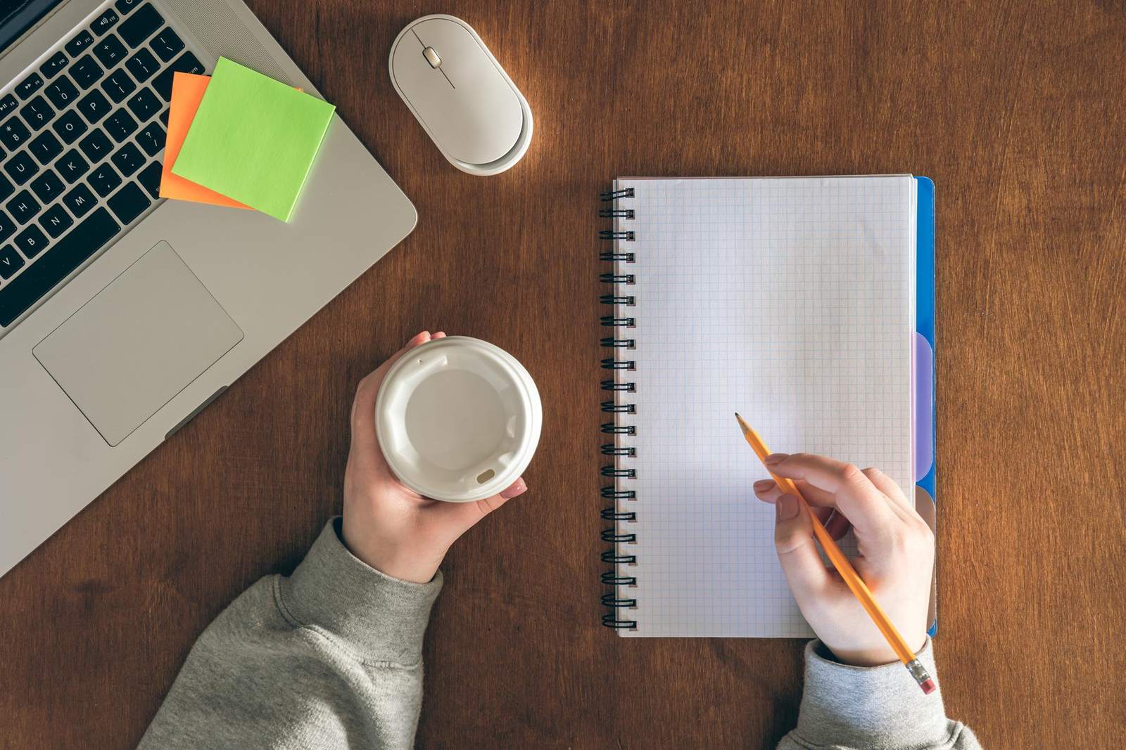 Overhead view of someone planning in a notebook beside a laptop and coffee