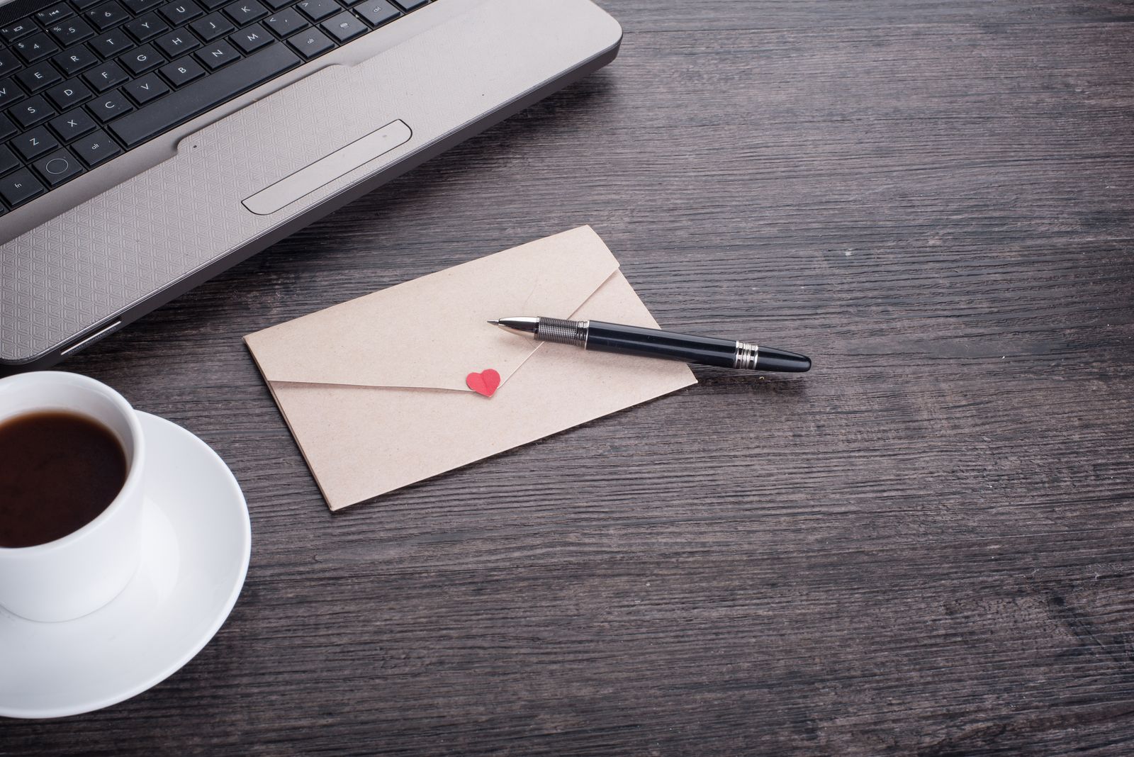A letter in an envelope with a pen and coffee on a dark desk