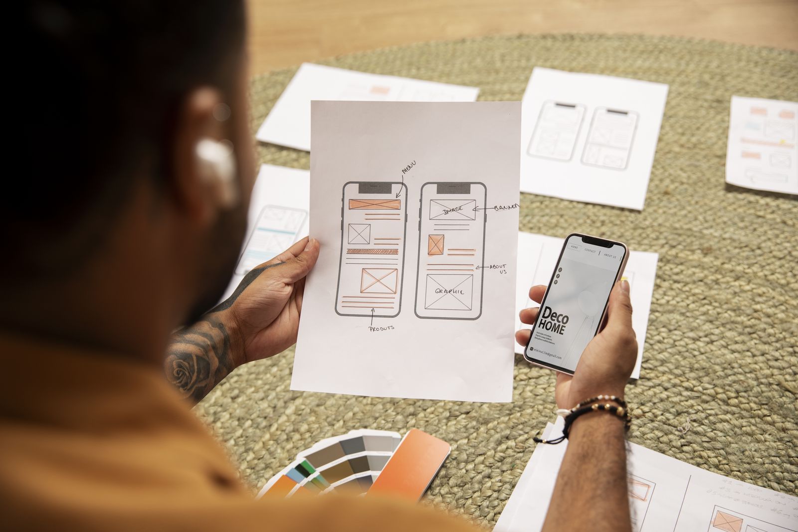 Designer holding a phone over paper mobile wireframes