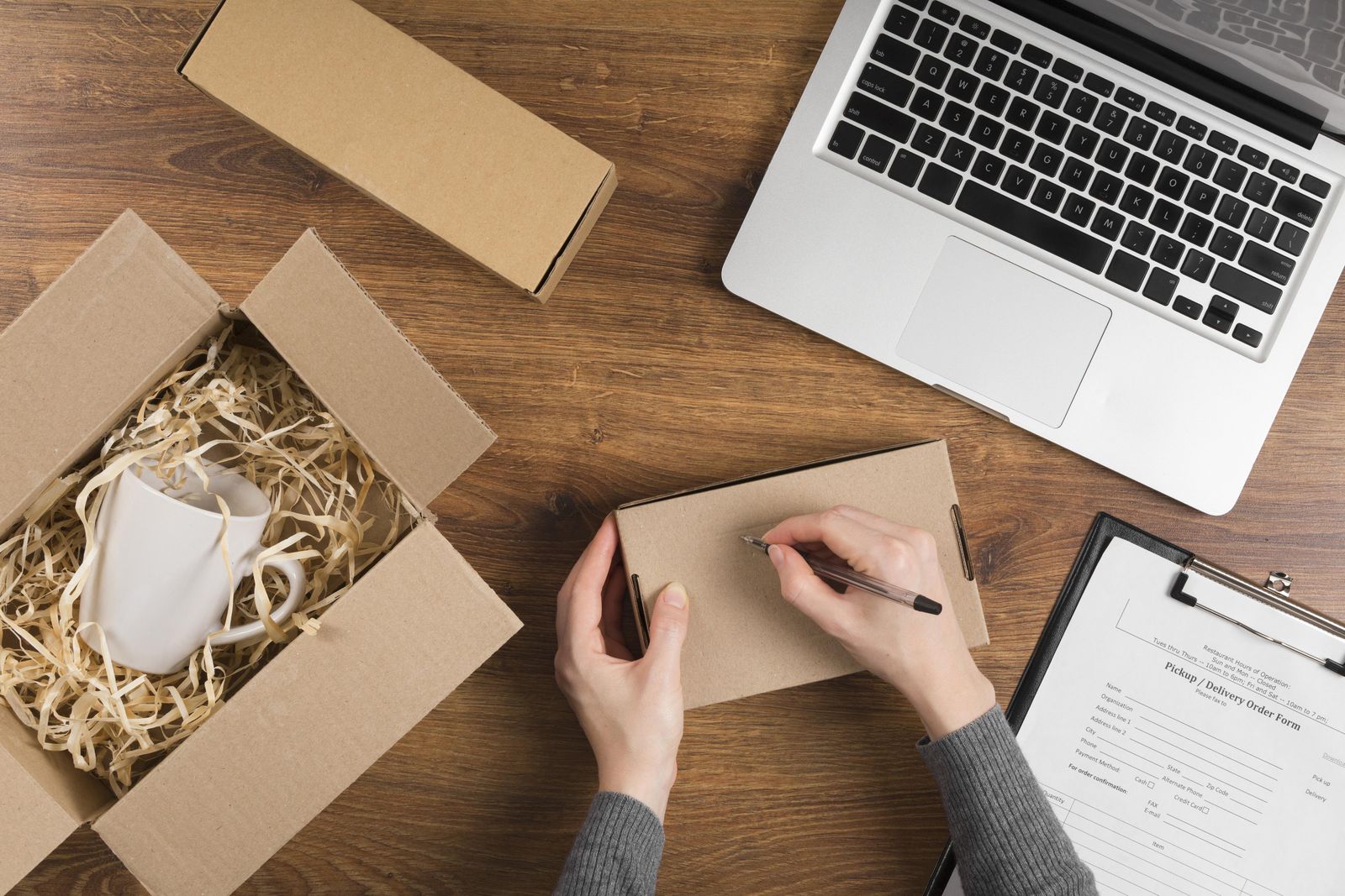 Hands packing a branded cardboard box next to a laptop