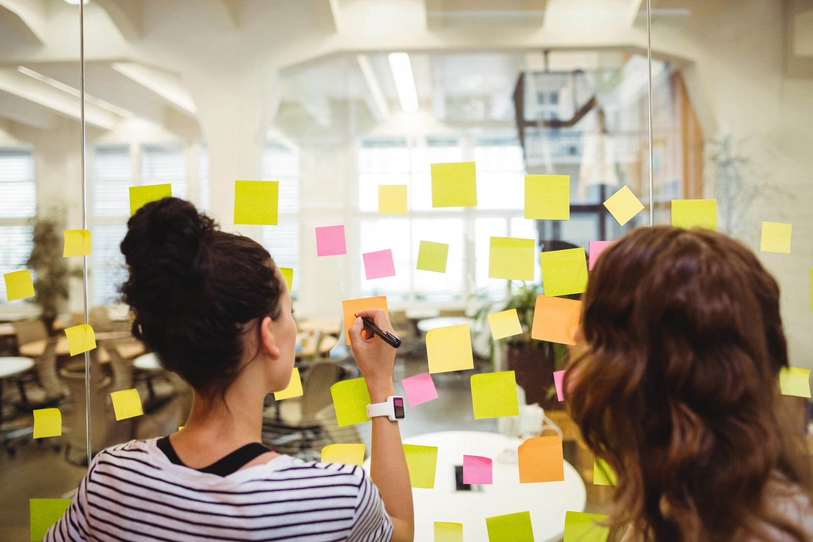 Two colleagues sticking notes on a glass wall during a workshop
